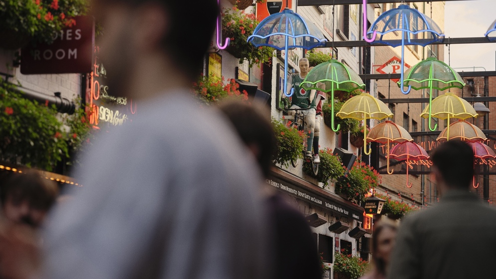The Duke of York, Belfast, beneath its colourful neon umbrella installation, with visitors walking through the narrow cobbled street.