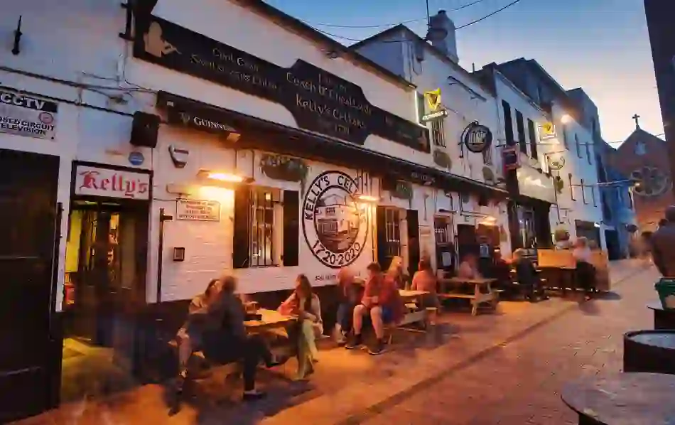 Kelly’s Cellars in Belfast, with people seated outside the historic whitewashed pub at dusk.