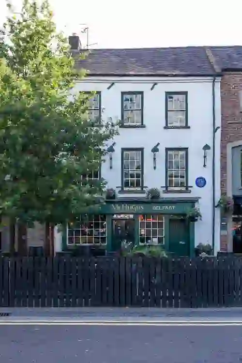 McHugh’s Bar in Belfast, a traditional white-fronted pub with green trim and hanging flower baskets.