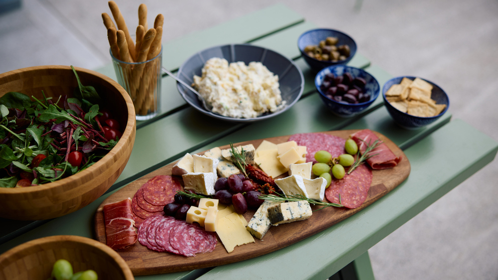 Charcuterie board with cheeses, cured meats and grapes beside salad and snacks at Wild Atlantic Glamping, West Cork.