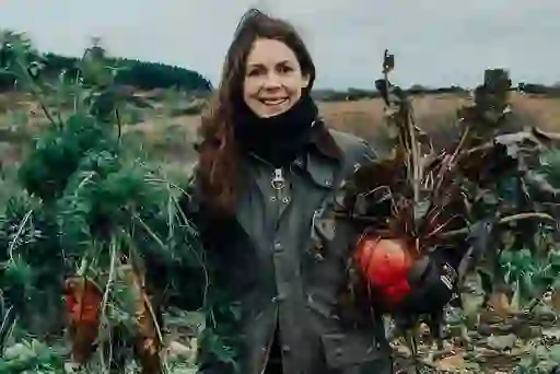 Donna sorridente che tiene carote e barbabietole appena raccolte nella fattoria di Broughgammon, nella contea di Antrim.