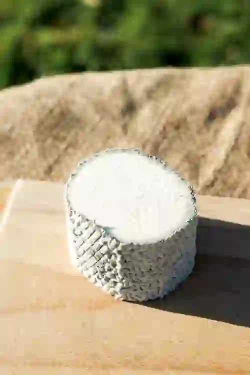 A round wheel of St Tola goat cheese resting on a wooden board outdoors.