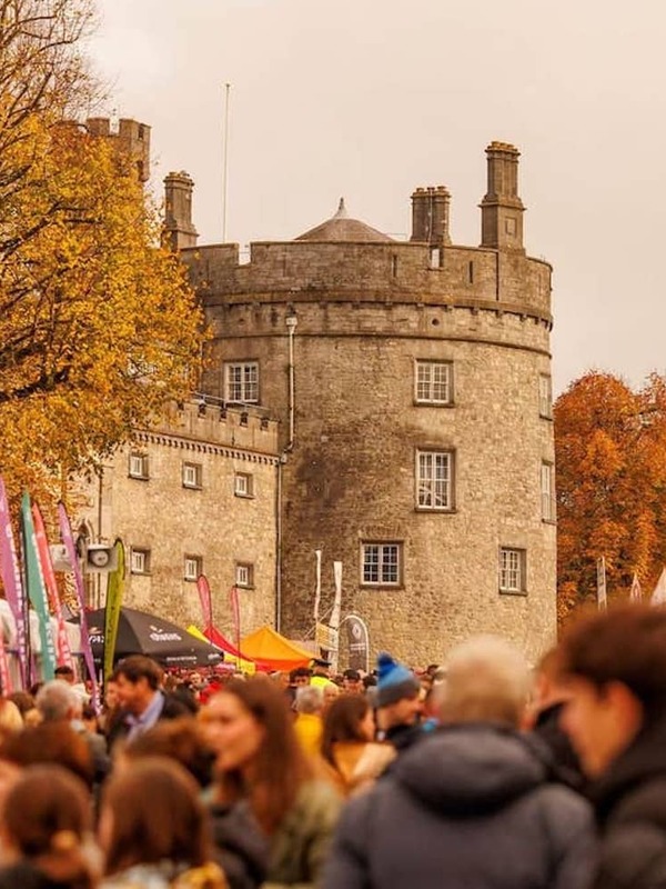 Menigtes bekijken kleurrijke eetkraampjes buiten het kasteel van Kilkenny tijdens het Savour Kilkenny Food Festival in de herfst.