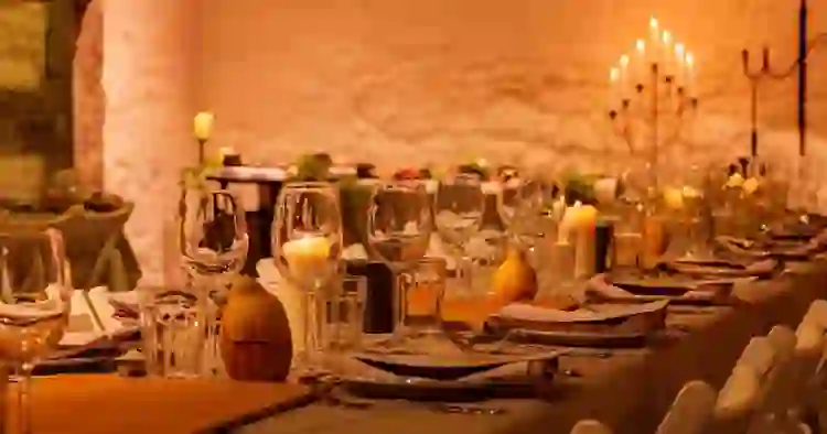 Candlelit dining tables set with glassware and place settings in a warm, rustic stone-walled venue.