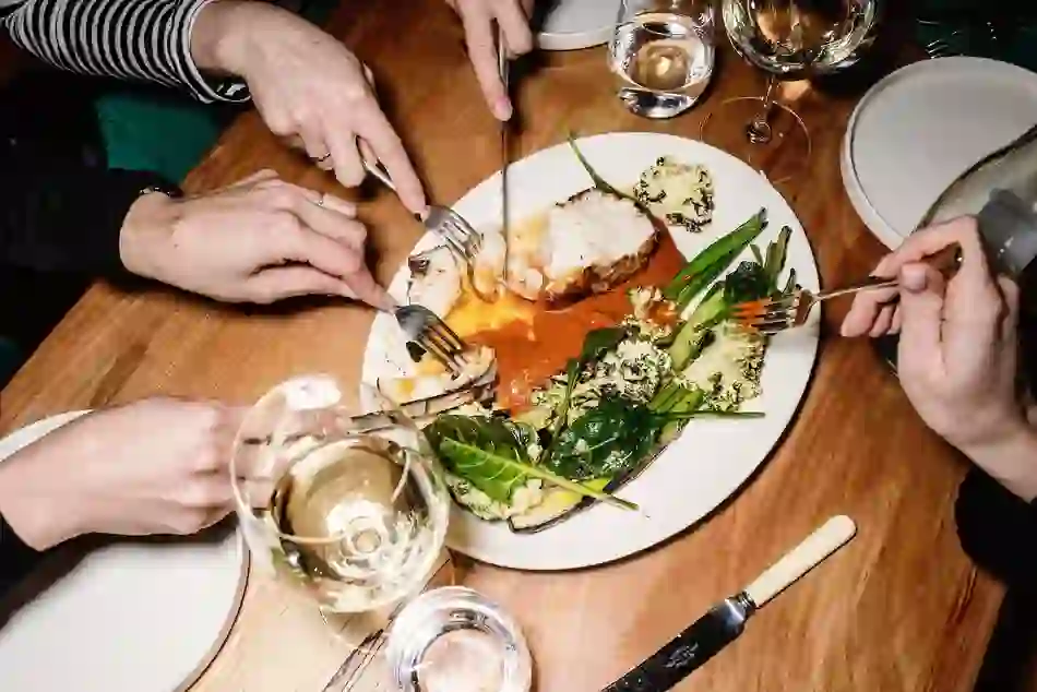 Diners share a seafood dish with grilled vegetables and wine at a wooden table.