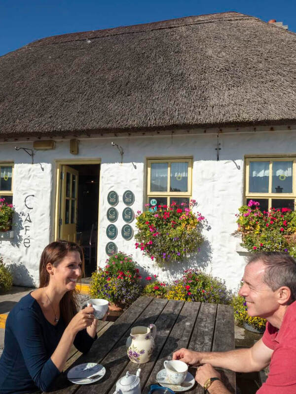 Het café Teach nan Phaidi met rieten dak op de Aran-eilanden, County Galway, met bloemstukken, waar bezoekers buiten van thee kunnen genieten.