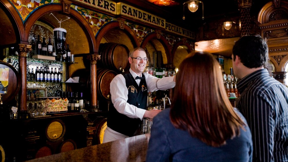 Un barman souriant servant des boissons dans un pub irlandais traditionnel au décor orné.