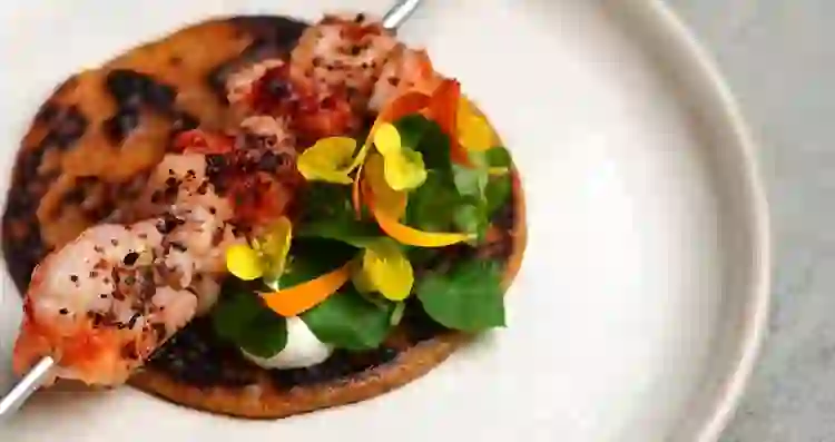 Gegrillte Garnelen mit essbaren Blüten und frischem Grün auf einem angeschwärzten Fladenbrot serviert im Dede, Grafschaft Cork.