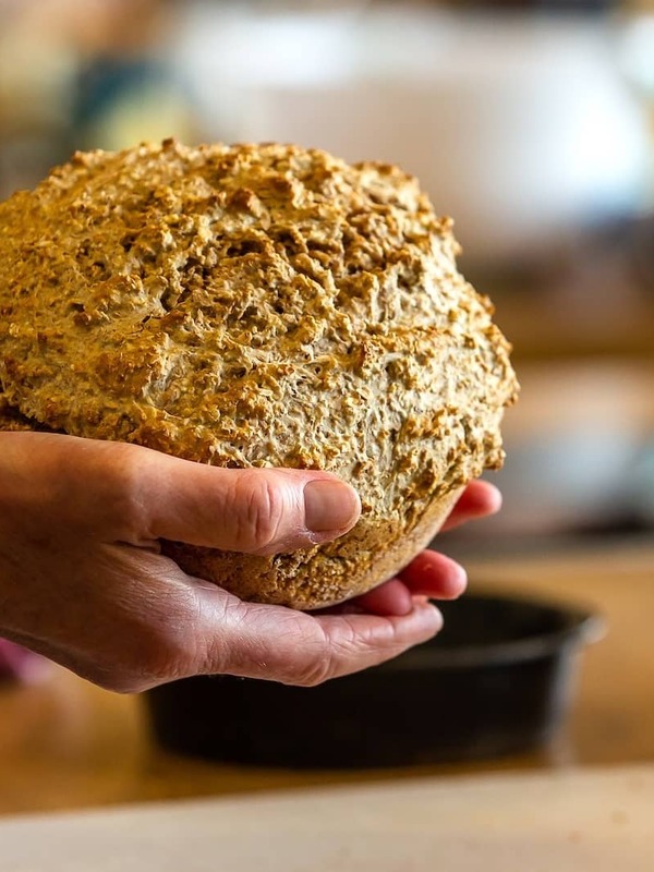 Hands holding a freshly baked loaf of traditional Irish brown bread in a rustic kitchen at Airfield Estate, Dublin.