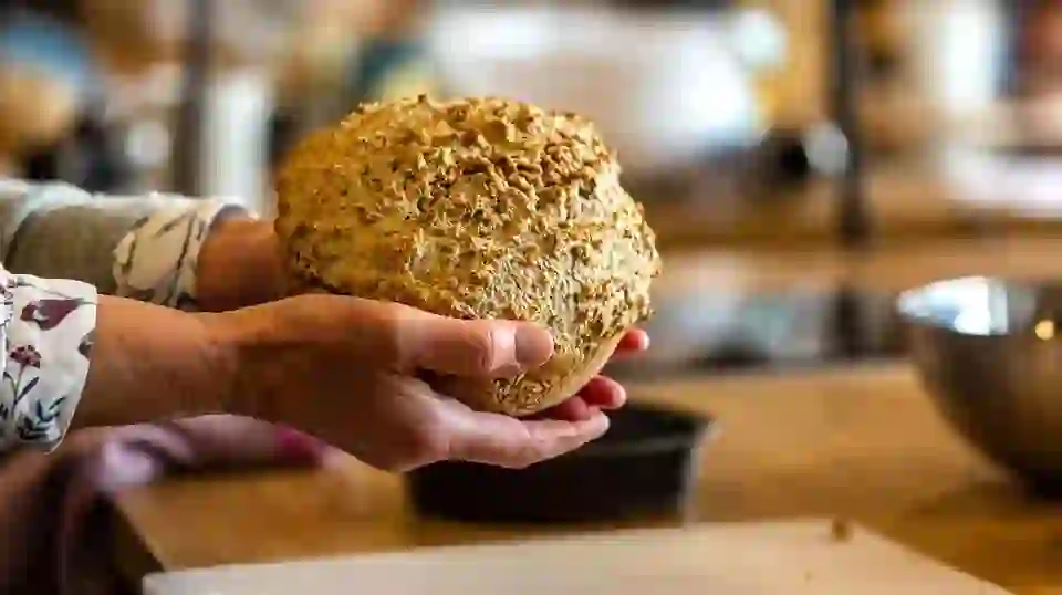 Hands holding a freshly baked loaf of traditional Irish brown bread in a rustic kitchen at Airfield Estate, Dublin.