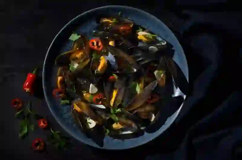 Steamed mussels in a dark bowl with chilli, garlic and fresh herbs.
