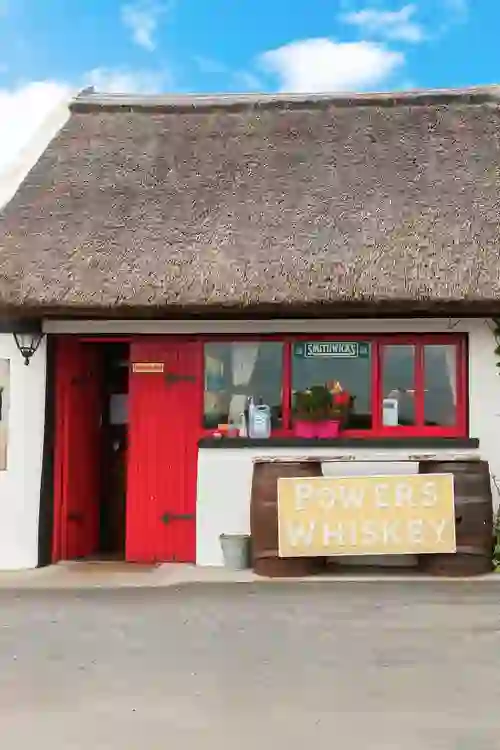 Een pub met een traditioneel rieten dak, felrode deuren en een Powers whiskey-reclamebord in Sligo.