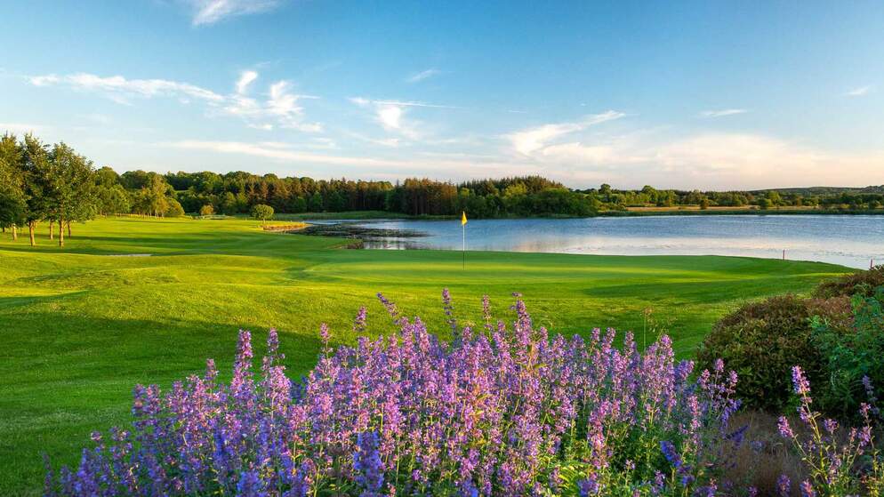 Scenic golf course in Ireland’s Hidden Heartlands with lakeside views and wildflowers in the foreground.