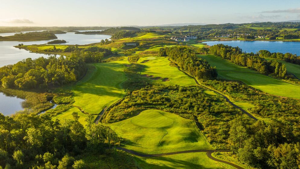 Scenic aerial view of Lough Erne Golf Resort with green fairways, lakes, and surrounding hills at sunset.