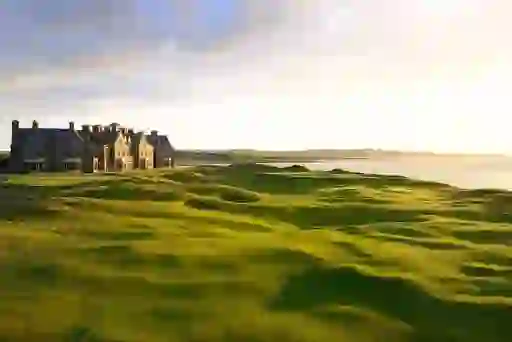 Luxury clubhouse overlooking Trump Doonbeg Golf Links in County Clare at sunset, with rolling dunes beside the sea.