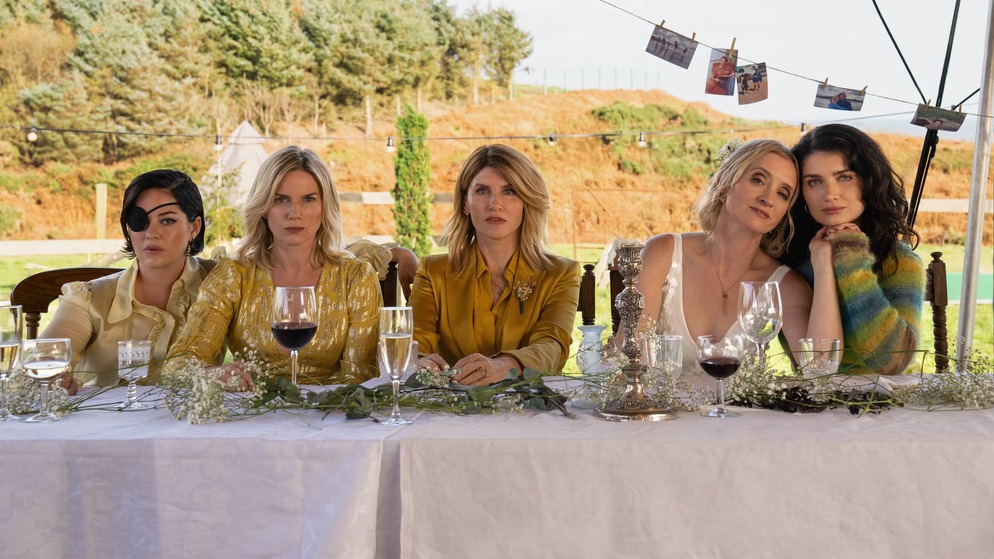 The Garvey sisters sit at a table in Bad Sisters, filmed in coastal Ireland locations.