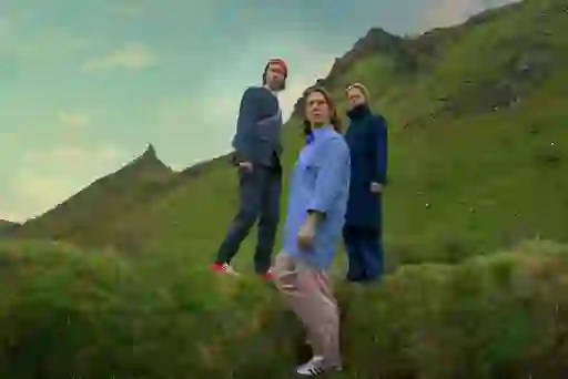 Still from How to get to Heaven from Belfast, showing three women on a hillside, looking off into the distance, with green mountains and a cloudy sky.