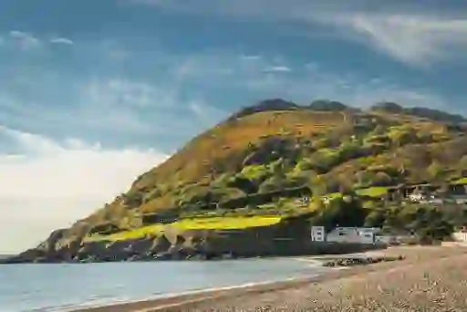 Sandy beach below a sunlit Bray Head with houses and trees beside a calm bay in Bray, County Wicklow.