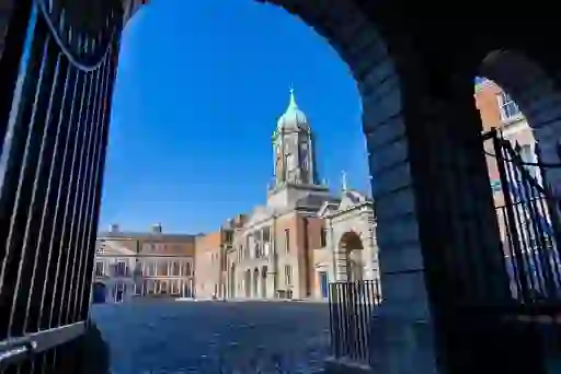 Dublin Castle courtyard framed by an archway, with the clock tower under a blue sky.