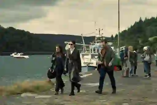 Three people walk along a harbour pier with fishing boats and hills behind them in Bodkin.