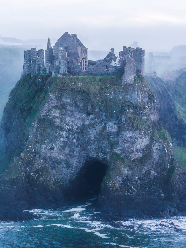 Ruined Dunluce Castle above the Atlantic Ocean in misty weather on the County Antrim coast.