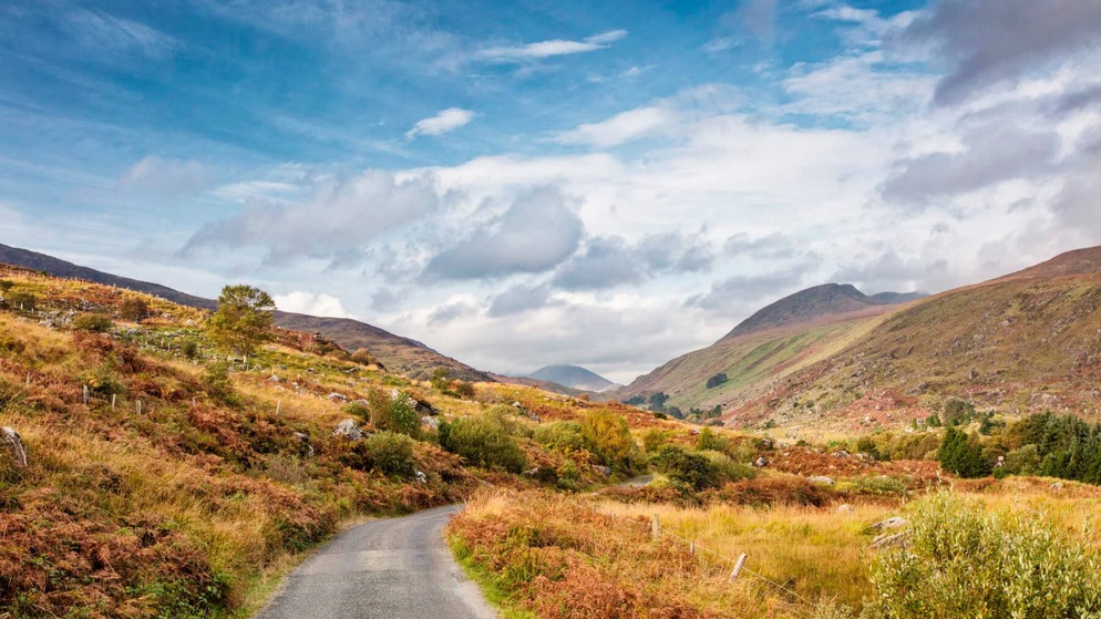Autumn colours fill a mountain valley on the Ring of Kerry beneath a dramatic cloudy sky.