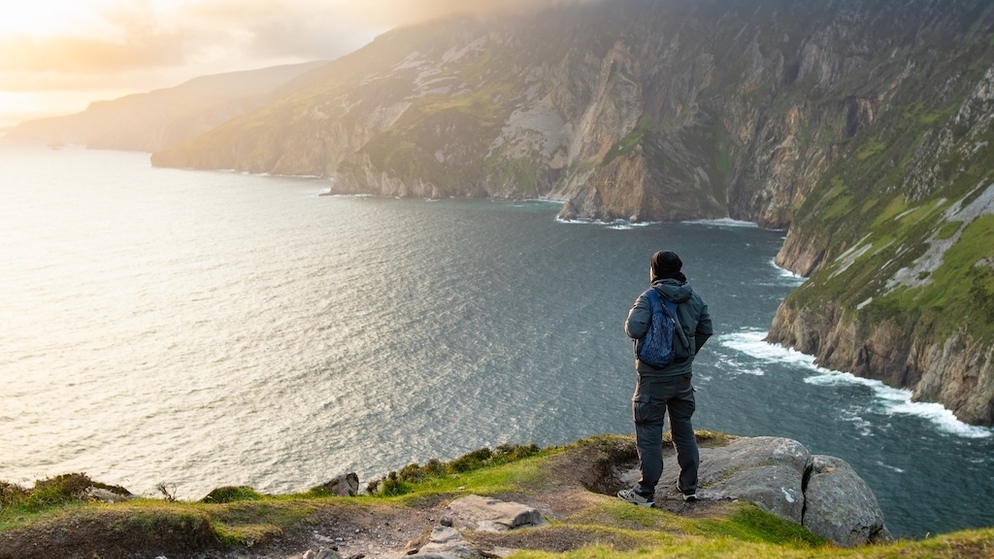 Hiker die op de rand van een klif staat met uitzicht op de dramatische kustlijn bij Slieve League, county Donegal.