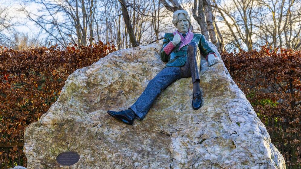 Oscar Wilde statue in Merrion Square Park, Dublin, pictured on a winter day with bare trees and blue sky behind.