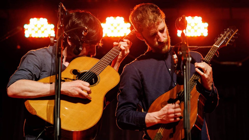 Deux musiciens de rock masculins se produisent sous des lumières rouges, mettant en valeur l'influence de l'Irlande sur la musique rock mondiale.