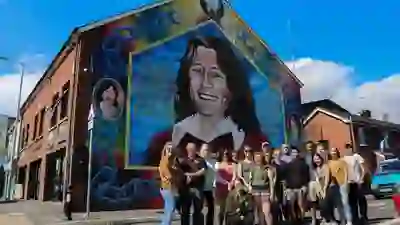 Un gruppo di visitatori posa davanti a un grande murale colorato in una via di Belfast.