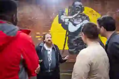 Una guida parla ai visitatori accanto a un grande murale su un muro di mattoni durante il Seedhead Arts Street Art Walking Tour a Belfast.