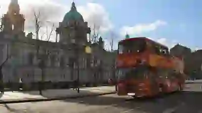 Un bus turistico rosso passa davanti al Belfast City Hall in una giornata soleggiata.