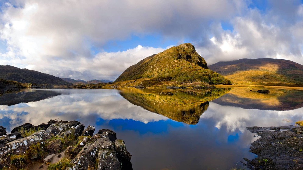 Sunlit mountain reflected in still waters at the Lakes of Killarney near the Gap of Dunloe, County Kerry.