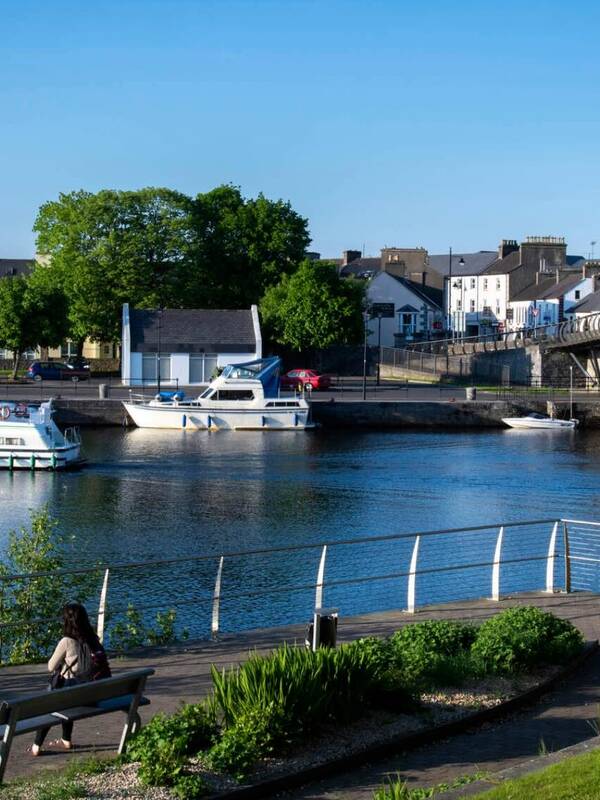 Carrick-on-Shannon town with boats moored on the River Shannon and stone bridge under clear blue sky.