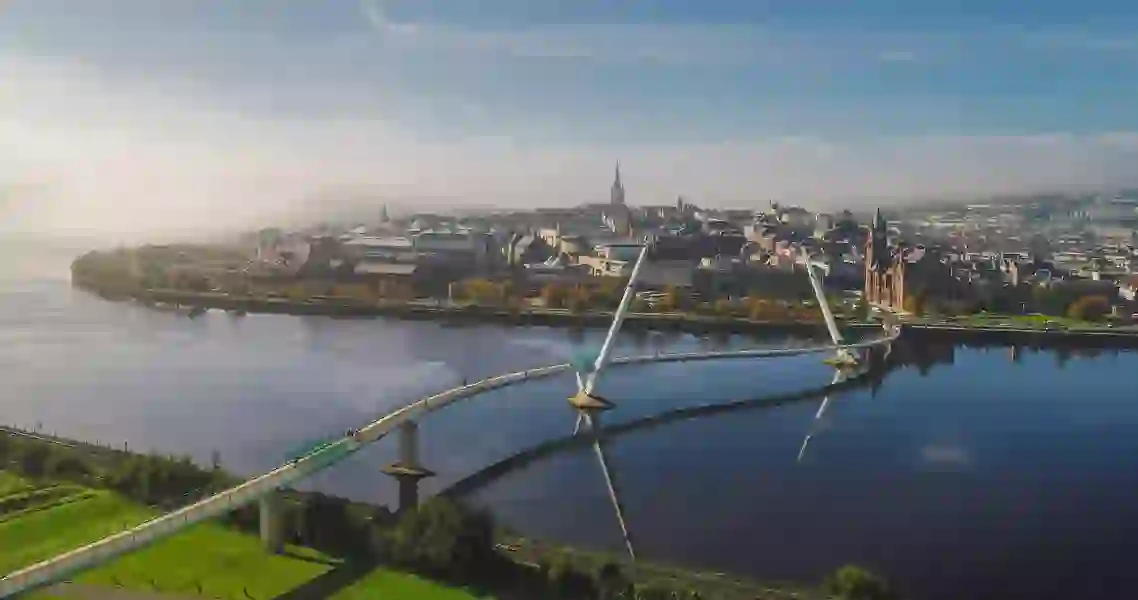 Aerial view of a bridge curving over a wide river towards a city skyline.
