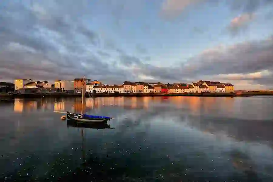 Reflections of colourful houses and a boat on calm evening water.