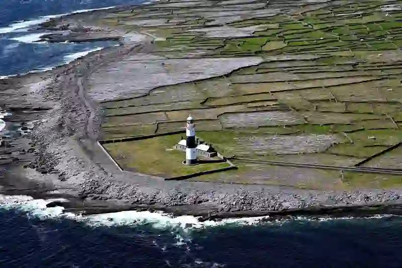 Black and white lighthouse surrounded by stone-walled green fields and a rocky coastline.