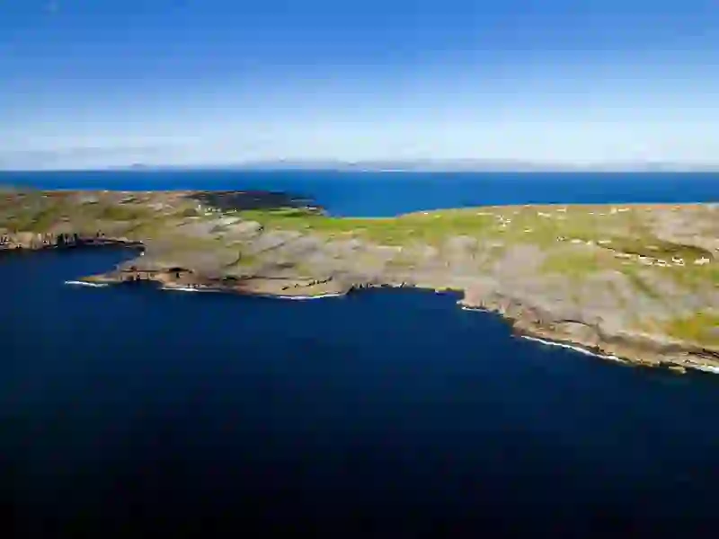 Rocky shoreline and patchwork fields of Inis Mór stretch toward the deep blue Atlantic Ocean under clear skies.