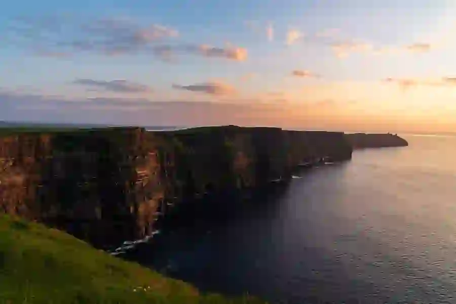 Towering sea cliffs stretch along the Atlantic coast, with the soft golden light of sunset reflecting off the water.