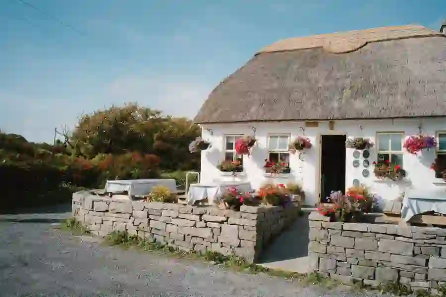 Restaurant in traditional Irish thatched cottage with blooming hanging baskets and outdoor seating.
