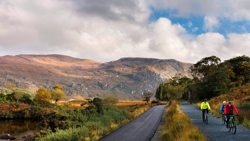 Una strada panoramica di montagna si snoda attraverso i promontori settentrionali di Donegal, con ciclisti che partecipano a un tour guidato sotto un cielo nuvoloso.