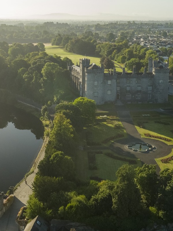 Aerial view of Kilkenny Castle surrounded by gardens and the city in soft morning light.