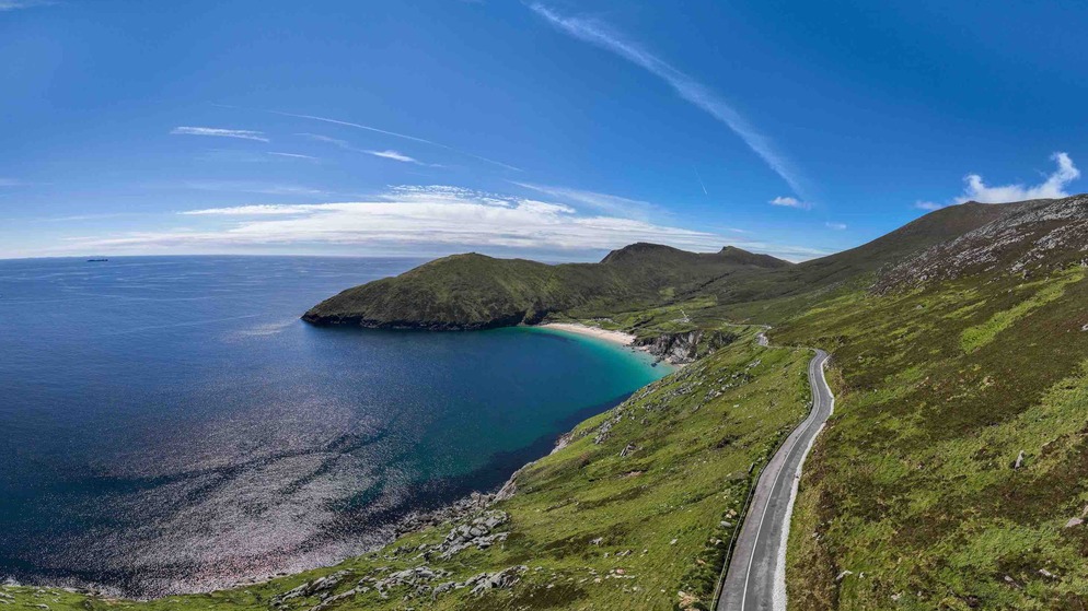 Route côtière courbée le long des falaises au-dessus de l'océan Atlantique sur le Wild Atlantic Way en Irlande, sous un ciel bleu avec des nuages légers.