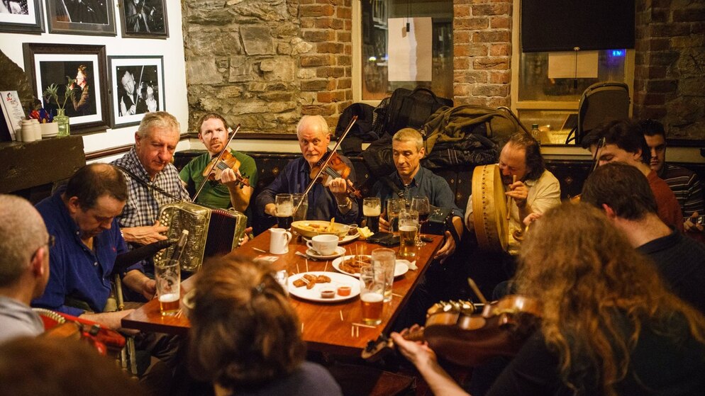 Traditiegetrouwe muzikanten spelen viool, bodhrán en accordeon rond een tafel in The White House, Limerick.