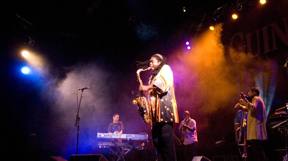 Il sassofonista suona su un palco fumoso al festival di jazz di Cork con la sua band e un'illuminazione vivace.