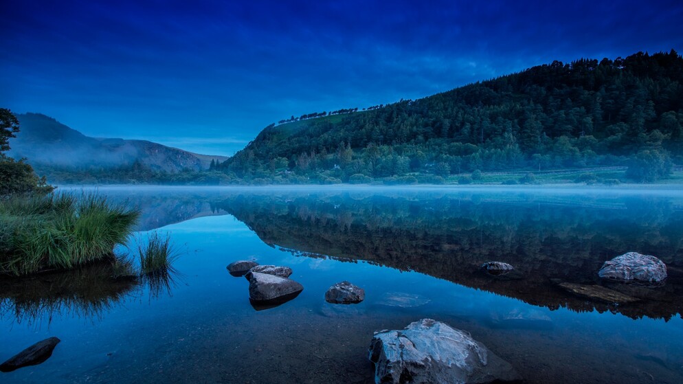 Misty morning reflection of forested hills on Upper Lake, Glendalough, County Wicklow.
