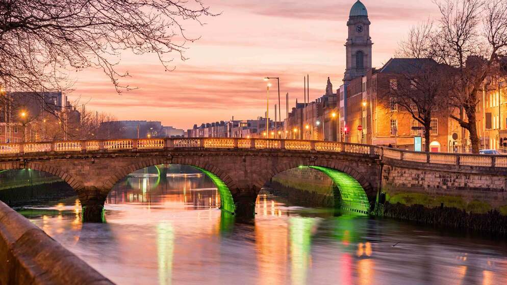 Vue du pont Ha'penny et de la rivière Liffey au coucher du soleil, avec des bâtiments de la ville et une flèche d'église dans le centre de Dublin.