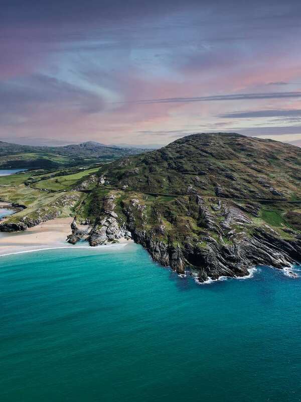 Aerial view of coastal cliffs and beaches in West Cork at sunset, with rivers winding through green fields.