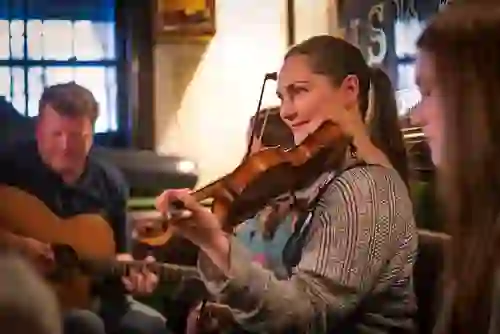 Musicians playing fiddle and guitar during a lively traditional music session in a Belfast pub.