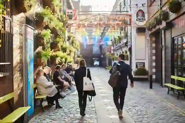 Mensen die door de Commercial Court in het Cathedral Quarter van Belfast lopen, onder kleurrijke hanglampen.